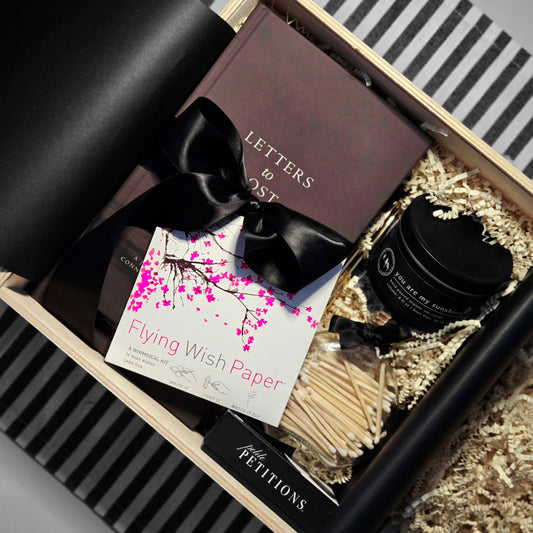Gift box with stationery items including a notebook, matches, and paper in a decorative setting.